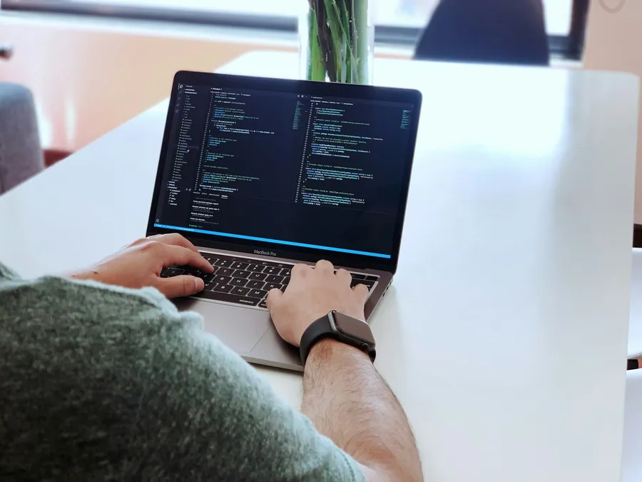 Hands typing on a laptop with code on screen